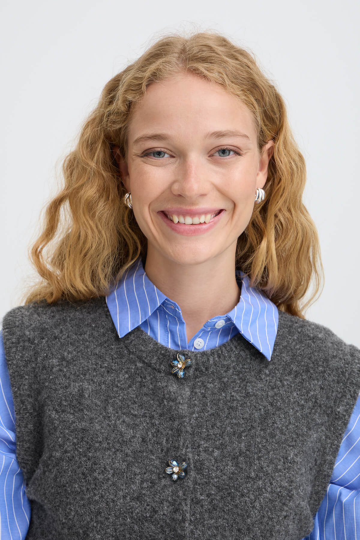 Close-up of a model wearing the b.young Omea vest over a striped shirt, showing the floral button detail