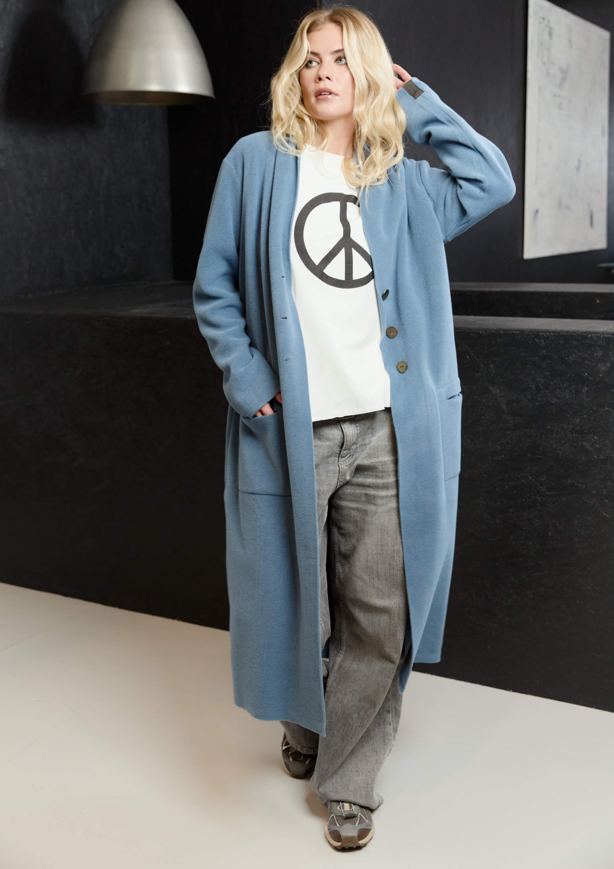 A woman models a long, light blue fleece cardigan.